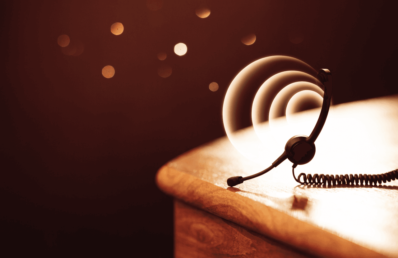 A headset on a warm desk, ringed by softly glowing sound waves.
